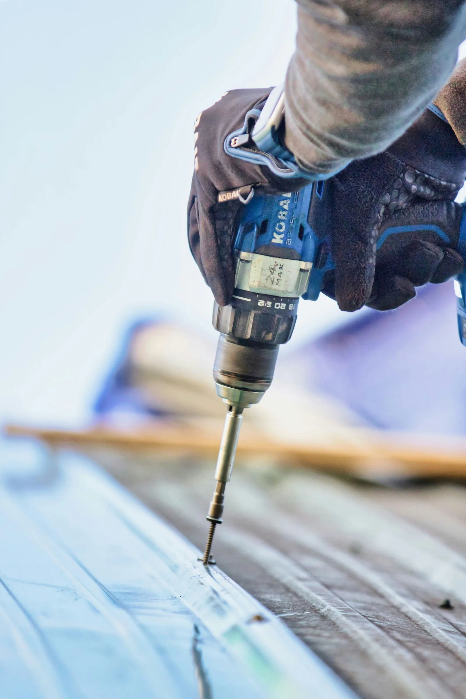 A roofer driving a screw into a metal roof panel